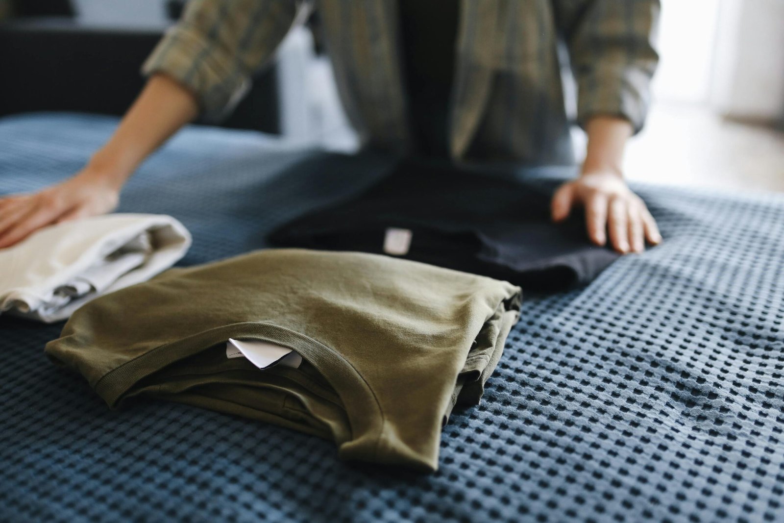 Hands folding T-shirts on a bed, showcasing household chores and casual apparel.