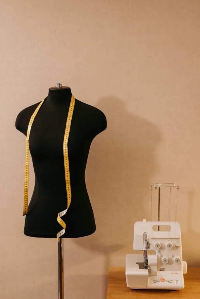 Black mannequin with a yellow tape measure and white sewing machine on a wooden table.