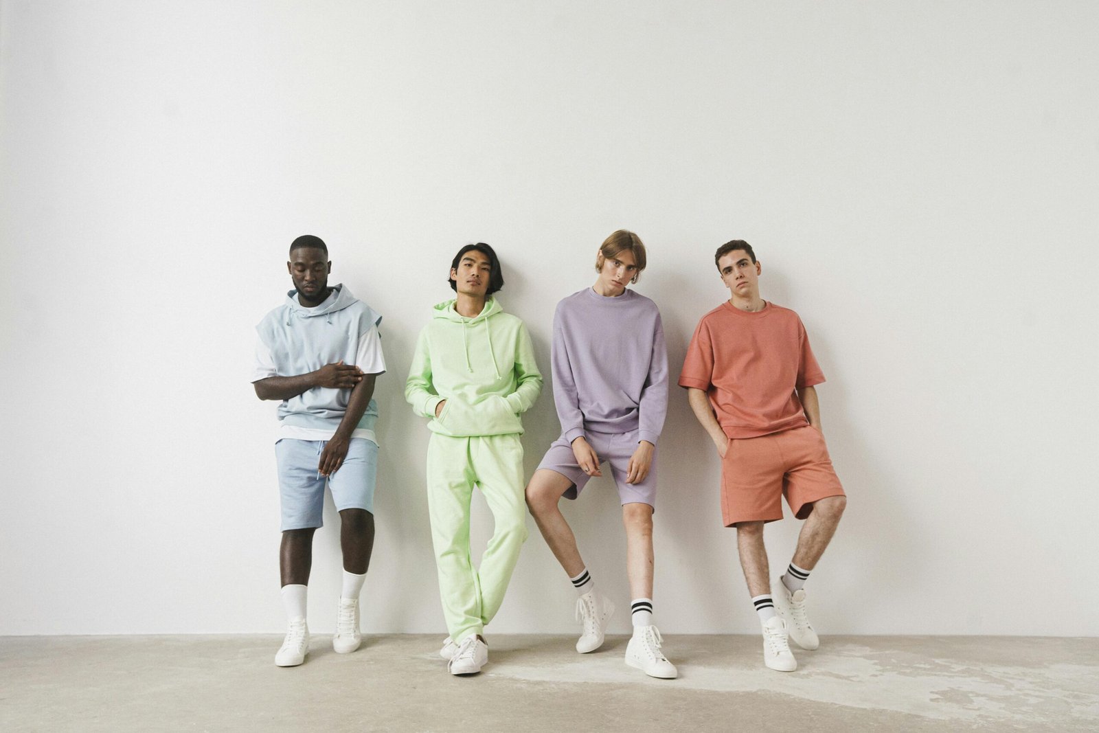 Group of stylish men in colorful pastel outfits posing against a white wall.
