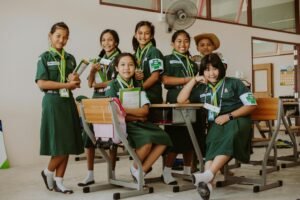 A group of smiling students in uniform posing together in a school classroom.