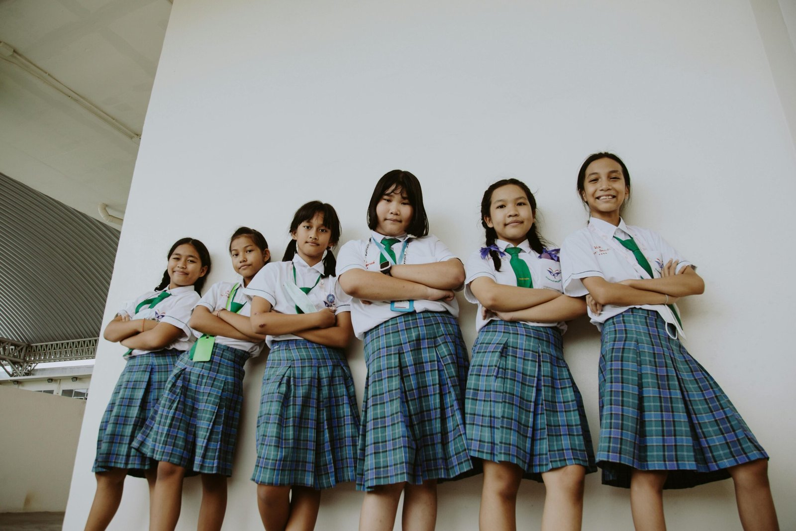 A group of cheerful schoolgirls in uniforms standing confidently against a wall.