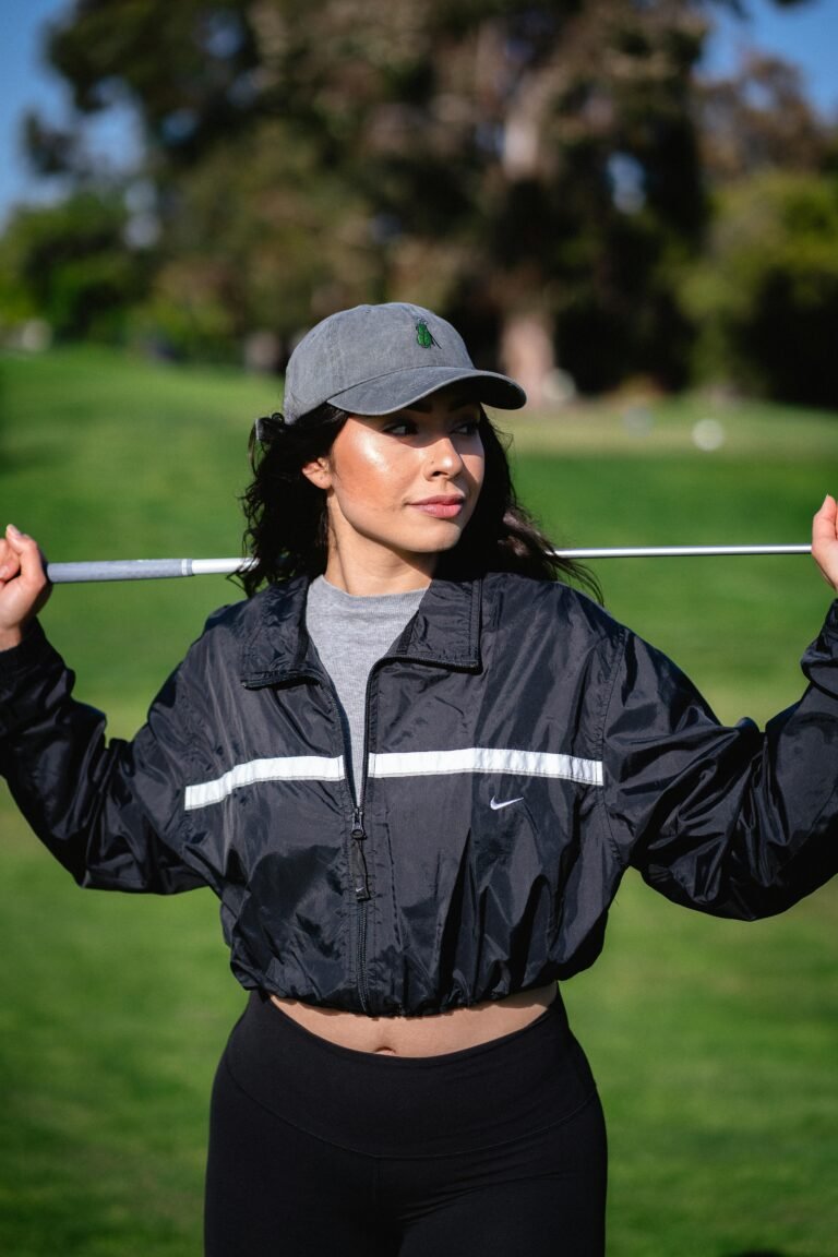 A young woman in sporty attire poses confidently with a golf club on a golf course.