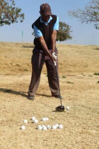 Golfer practicing swing in Soweto on dry grass field, sunny day.