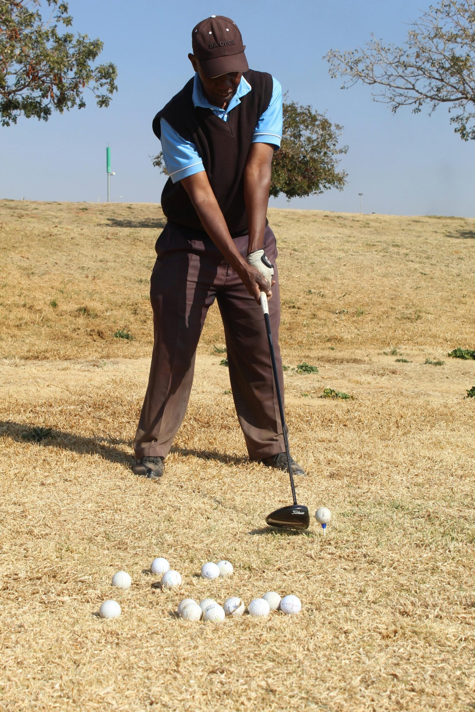 Golfer practicing swing in Soweto on dry grass field, sunny day.