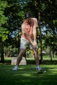 A man in a pink shirt prepares to swing his golf club on a sunny golf course.