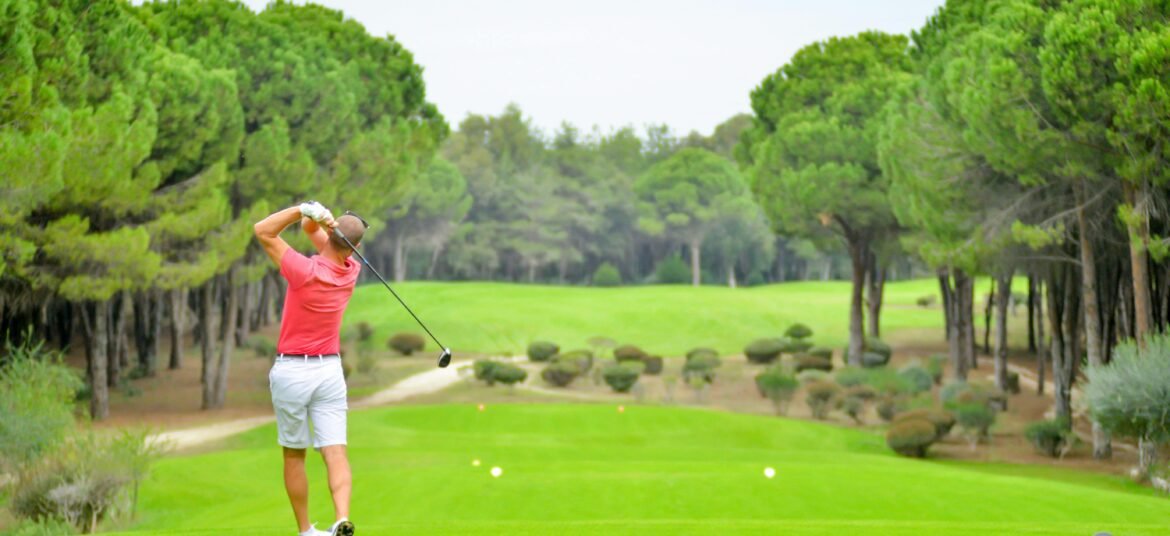 Back view of a golfer swinging a club on a lush golf course in Antalya, Türkiye.