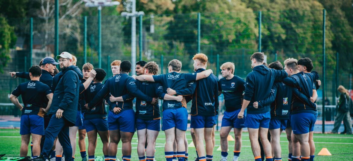 Rugby team gathers in a huddle on green field, preparing for a match, showcasing team spirit and sportsmanship.