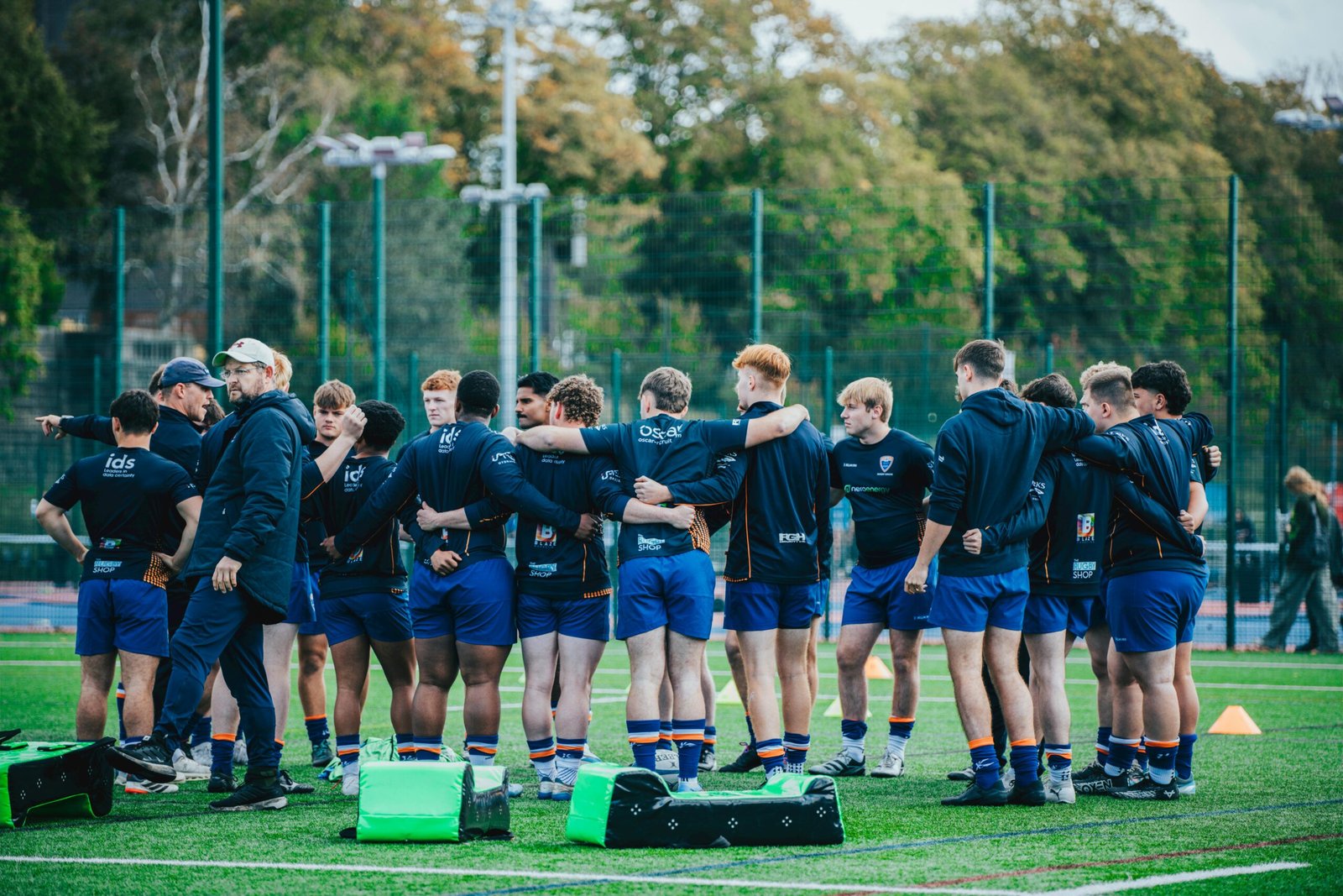 Rugby team gathers in a huddle on green field, preparing for a match, showcasing team spirit and sportsmanship.