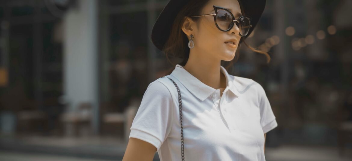 Fashionable woman in a white polo shirt, sunglasses, and black hat outdoors, exuding style and confidence.