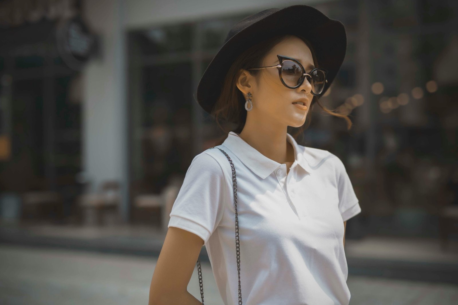 Fashionable woman in a white polo shirt, sunglasses, and black hat outdoors, exuding style and confidence.