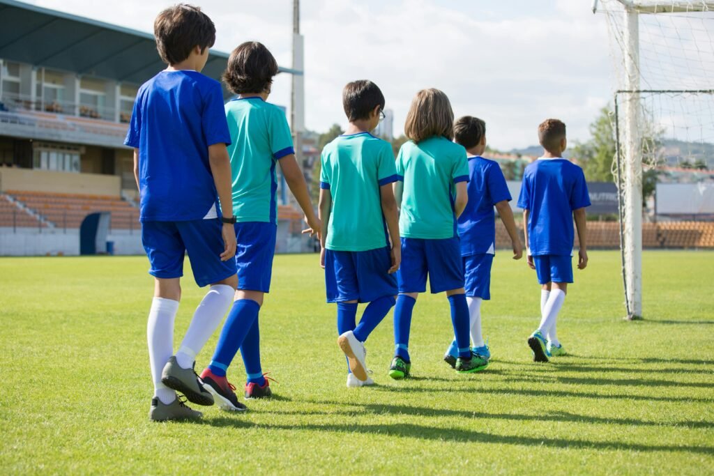 Children in football uniforms walking on a sunny field, preparing for training.