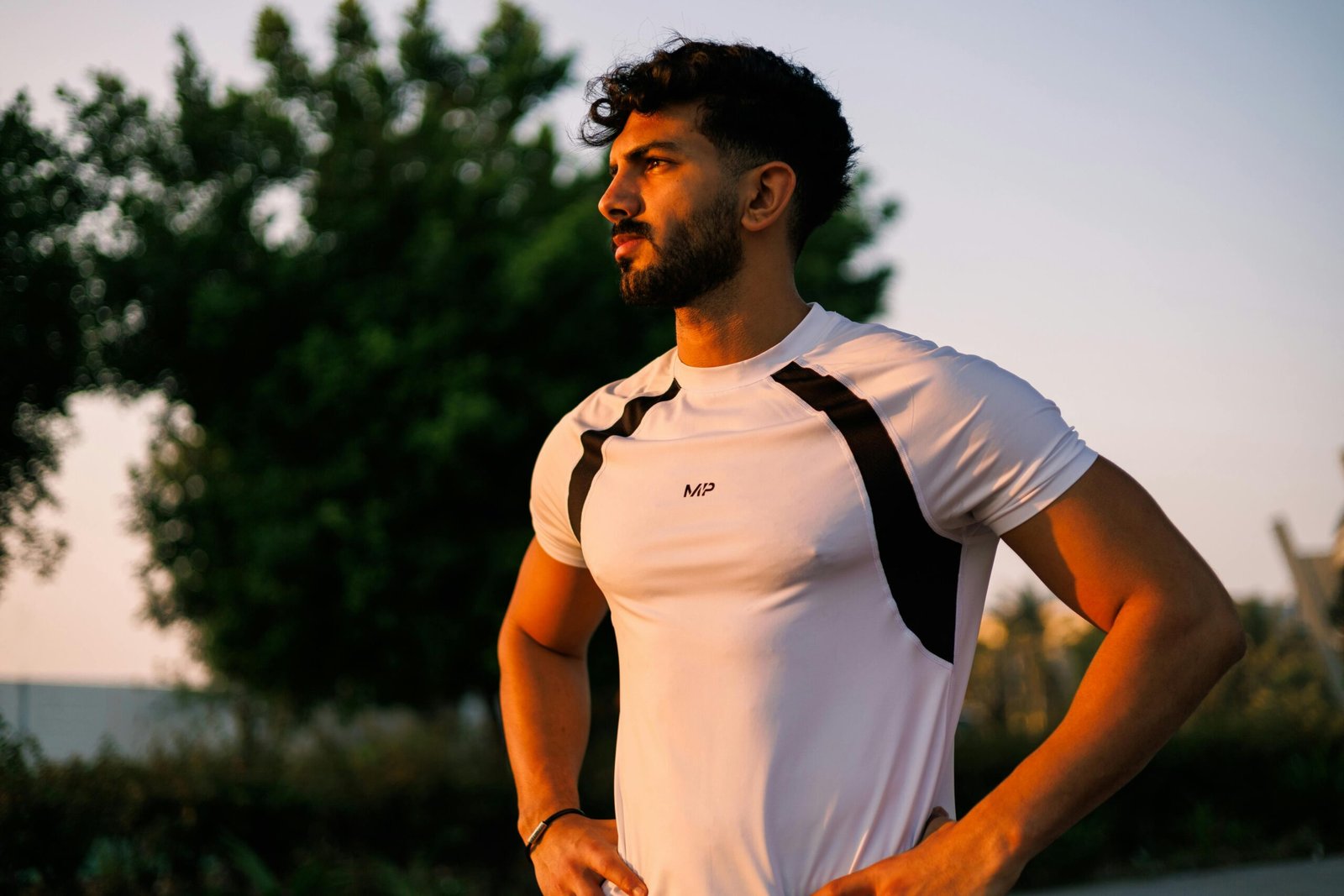 Athletic man in a white shirt stands confidently during sunrise in Jeddah, Saudi Arabia.