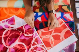 Vibrant fabric samples displayed with hands selecting colors on a table.