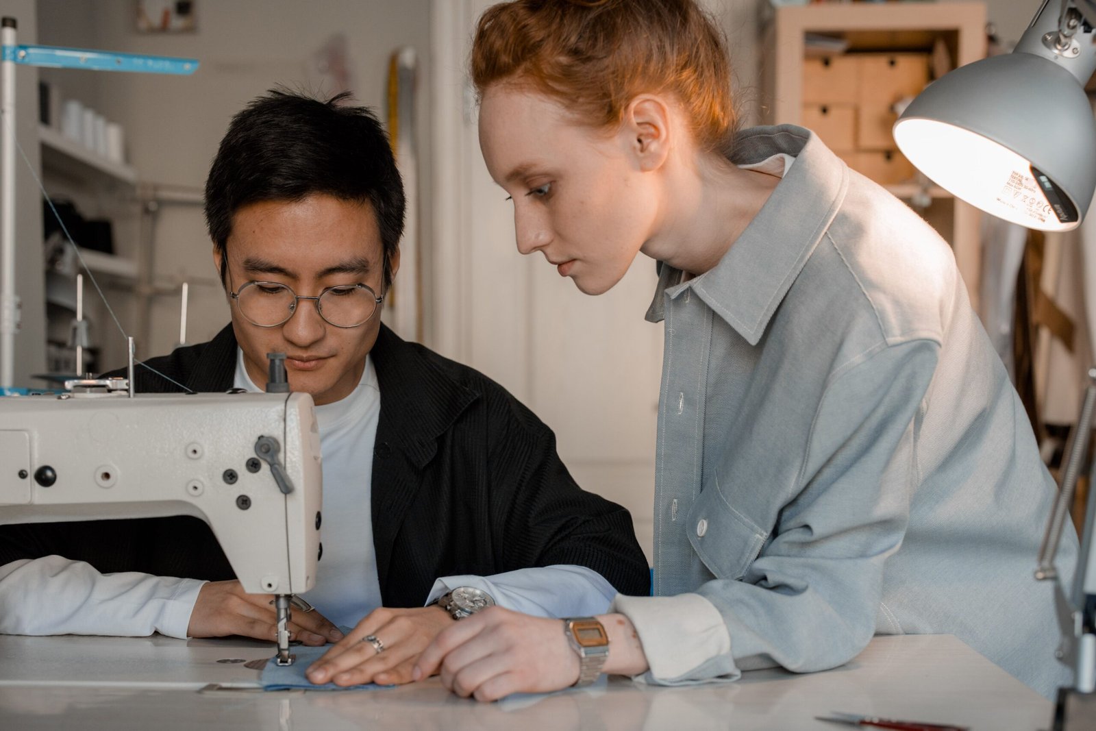A man and woman collaborating at a sewing machine in a workshop.