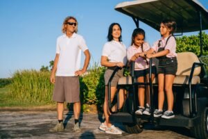 Family smiling and standing around a golf cart on a sunlit day outdoors.