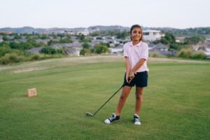 A smiling girl holding a golf club on an outdoor golf course, enjoying a sunny day.