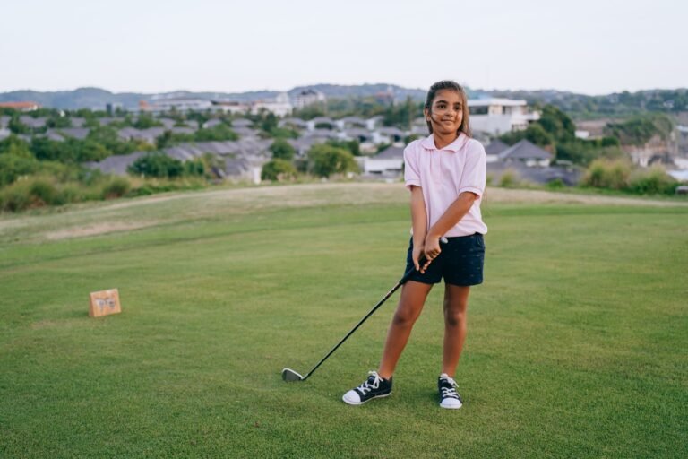 A smiling girl holding a golf club on an outdoor golf course, enjoying a sunny day.